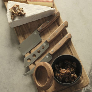 Morso cheese knives arranged on a wooden board with soft cheese, bread and walnuts.