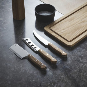 Set of three Morso cheese knives on a dark benchtop beside a wooden board.