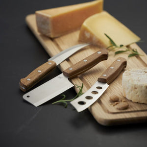 Morso cheese knives on a wooden board with assorted cheeses and herbs.