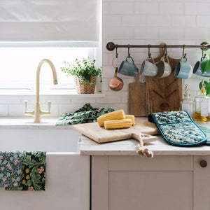 Kitchen counter with Leicester Wallpaper print tea towels and oven mitt, corn on the cob, and mugs hanging above.