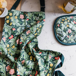 Close up of the Museums & Galleries Leicester Wallpaper apron showing its green floral print, with the matching oven glove and kitchen items nearby.