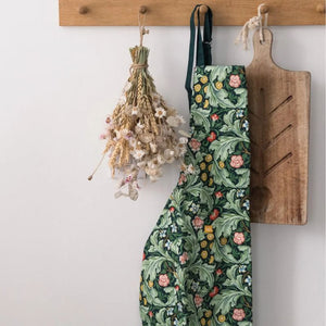 Green floral Museums & Galleries Leicester Wallpaper apron hanging from a wooden peg next to dried flowers and a chopping board.