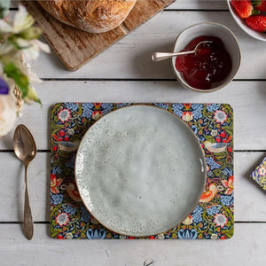 Table setting with a William Morris Strawberry Thief placemat, ceramic plate, and bowl of jam on a wooden table.