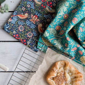 V&A Morris Designs tea towels beside a cup of tea and croissant.