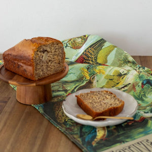 NZ Native Birds Tea Towel displayed in a kitchen scene with a banana loaf.