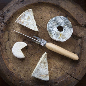 Opinel cheese knife and fork displayed on a rustic wooden board with cheese wedges.