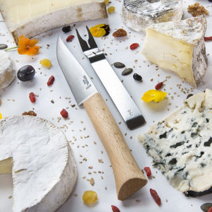 Flatlay of Opinel cheese knife and fork surrounded by assorted cheeses.