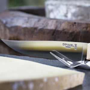 Close-up of Opinel cheese knife slicing soft cheese on a wooden board.