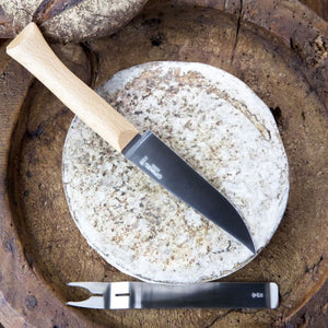 Opinel cheese knife placed on top of a round soft cheese on a wooden serving board.