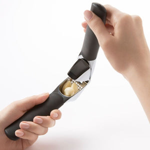 Hand holding the OXO Good Grips Garlic Press with cloves of garlic inside on a white background