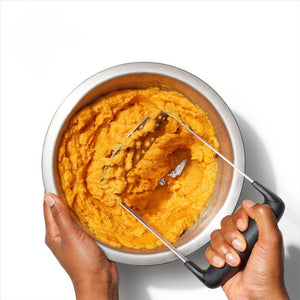 Person using the OXO Good Grips Smooth Potato Masher to mash sweet potato in a metal bowl.