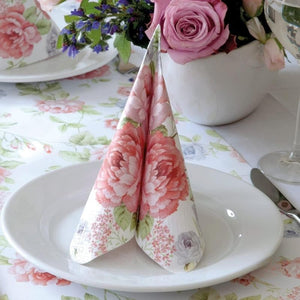 PAW Julietta Paper Napkins styled folded on a white plate with a vase of roses in the background.