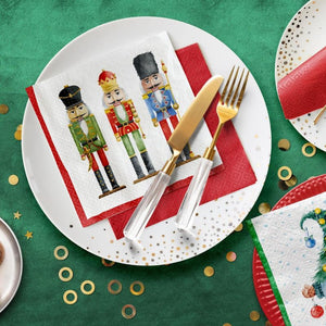 A styled tabletop setting with PAW Paper Napkins in the Nutcrackers Soldiers design,  and clear-handled silver cutlery, on a green tablecloth with gold confetti.