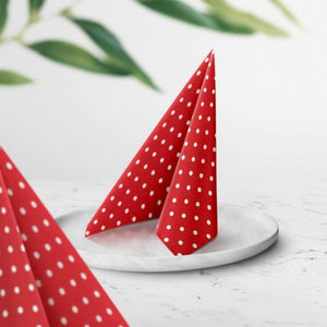 PAW Red Dots Paper Napkins shown folded on a white plate on a stone table.