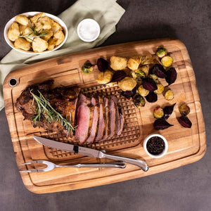 Sliced roast lamb displayed on an acacia carving board with roasted vegetables and carving utensils.