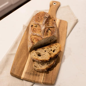 Peer Sorensen Paddle Serving Board - acacia serving board holding a loaf of bread and several slices.