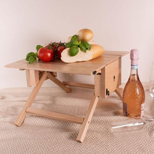 Folding wooden picnic table set up with food, wine bottle, and picnic accessories