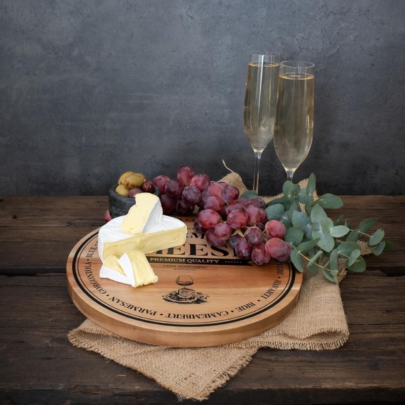 Peer Sorensen round wooden cheese board with brie, grapes, and champagne flutes on a rustic wooden table.