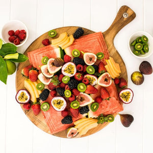 Round wooden serving board by Peer Sorensen with fresh fruit displayed on a white table