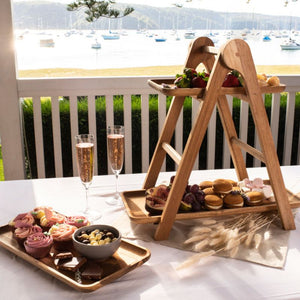 Acacia wood three tiered serving platform displayed outdoors with champagne and assorted appetisers.