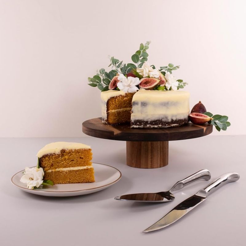 Peer Sorensen Acacia Cake Stand displaying iced cake and slice on plate with figs and foliage decorations