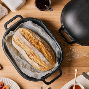 Loaf of bread in the Pyrolux Pyrocast Bake & Roast Set on a wooden table with a jar of jam and a black pot.