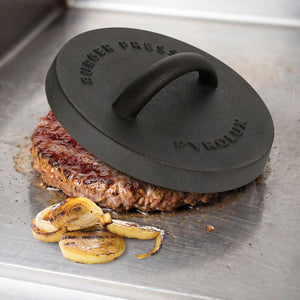 Pyrolux Pyrocast Burger Press styled on top of a pattie with onions on a metal surface.