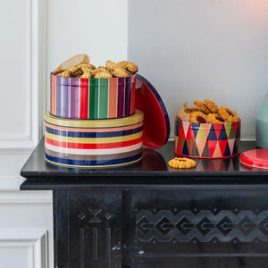 Colourful striped and geometric patterned cookie tins with home baking inside on a black mantlepiece.