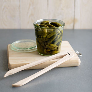 Roger Orfèvre French Beechwood Cornichon Tongs shown next to a jar filled with small gherkins.