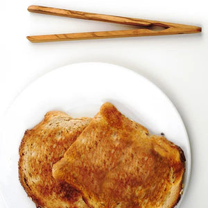 RSVP Olive Wood Toast Tongs styled next to a piece of toast on a white plate