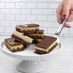 Person holding the RSVP Stainless Steel Brownie Spatula with a caramel slice over a cake stand.