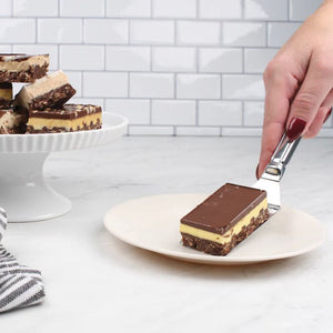 RSVP Stainless Steel Brownie Spatula holding a piece of caramel slice above a white plate.