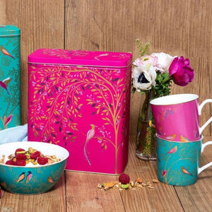 Sara Miller Chelsea Larder Tin styled next to a teal bowl, stacked teal and pink mugs, and a vase of flowers in the background.