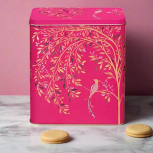 Sara Miller Chelsea Larder Tin set on a marble surface against a pink wall. Two small round biscuits sit in front of the tin.