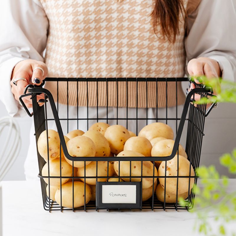 Person holding Seymours black wire stacking basket filled with potatoes