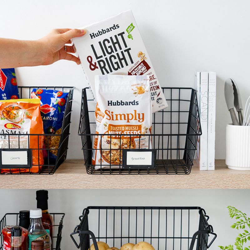 Person reaching into black wire basket with cereals and pantry items on shelf