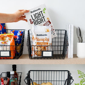 Person reaching into black wire basket with cereals and pantry items on shelf
