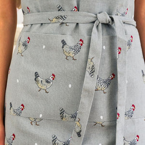 Close-up of the Sophie Allport Chicken Apron, a light gray apron with a printed pattern of chickens and white dots, featuring a tie waist belt.