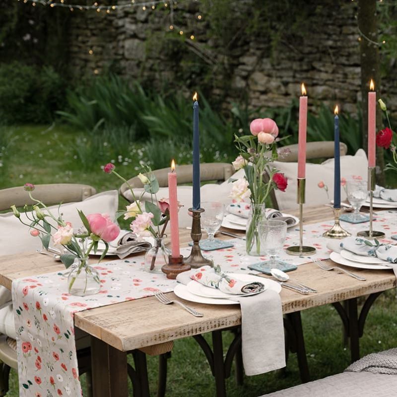 Sophie Allport Poppy Meadow cotton table runner and napkins on an outdoor wooden table with candles and flower.