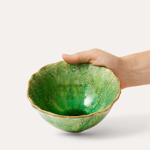 Hand holding a seaweed green Sthal Arabesque breakfast/soup ceramic bowl with intricate patterns and reactive glaze, shown on a white background.