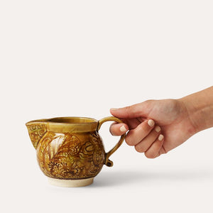 Hand holding the Sthal Arabesque Creamer in Pineapple colour against a white background.