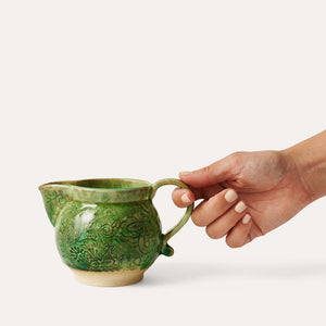 Hand holding Sthal Arabesque Creamer in Seaweed green against a white background.
