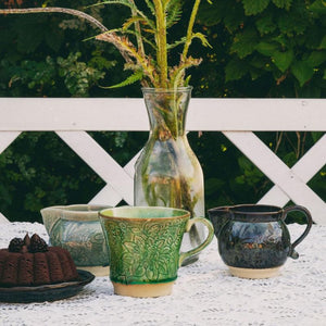 Sthal Arabesque Tea Mug in Seaweed shown on a white table with cake and other ceramics from the Arabesque range.
