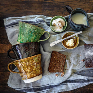 Stack of Sthal Arabesque tea mugs on tea towel with creamer and butter and garlic in dip bowls and bread nearby.