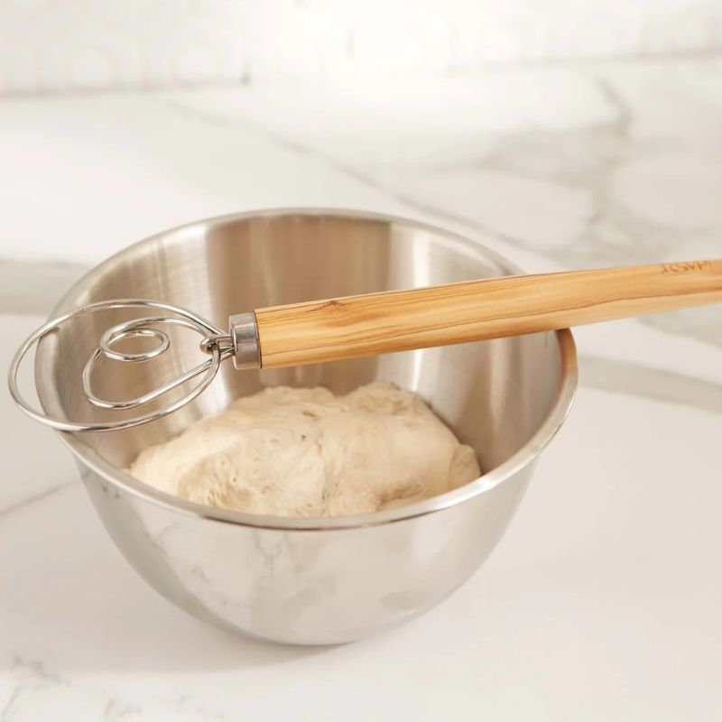Danish dough whisk resting on a stainless steel mixing bowl.