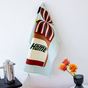 100%NZ Taste of Kiwi Tea Towel hanging from a hook in a kitchen - Vogels bread icon showing.