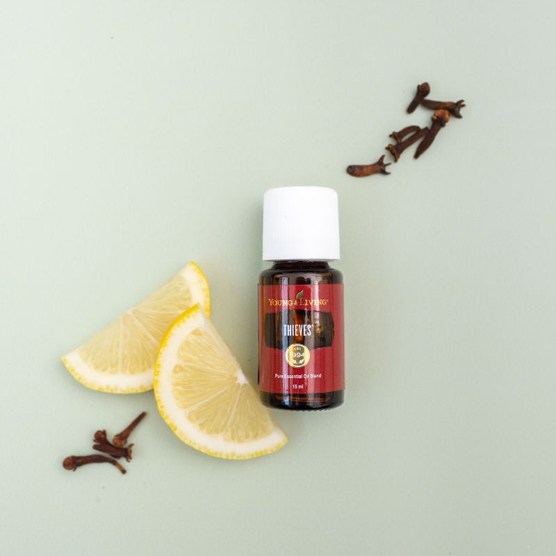 Young Living Thieves essential oil bottle with lemon slices and cloves on a light green background