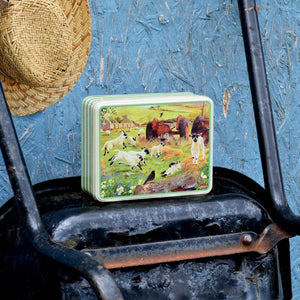 The Tracy Hall Wooly Jumpers Biscuit Tin on a wheelbarrow with straw hat behind