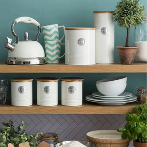 Kitchen shelves with cream cookie storage, pasta canister and tea, coffee, and sugar canisters from the Typhoon Living collection - shown with a kettle, plates and bowls against a teal wall.