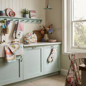 Ulster Weavers Cool Cats collection styled in a kitchen with soft green cabinets, flowers, and beige walls.
